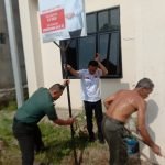 Babinsa Serka Armen Bantu Staf Kelurahan 11 Ulu Dirikan Plang Banner PMI